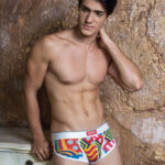 Model wearing Groovin' Cup boxer in bold geometric print – stylish men’s underwear with colorful patterns and white waistband, posing against a textured wall.